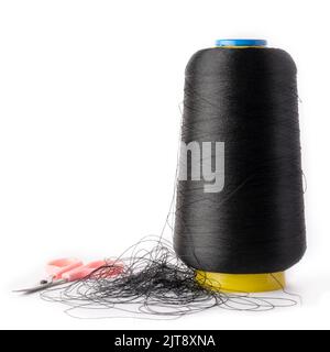 spool of black color sewing thread used in fabric and textile industry with an embroidery pair of scissors, isolated on white background Stock Photo