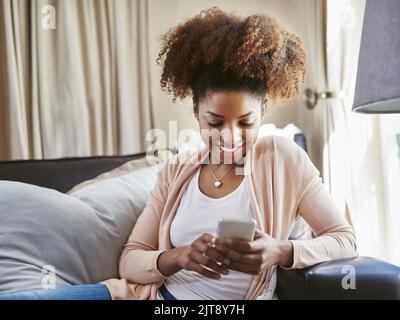 Keeping in contact. an attractive young woman using her cellphpone while chilling at home on the sofa. Stock Photo
