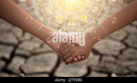 Young boy and girl holding hands in the dried soil with the sun light passing through the hands have astrological symbols. Stock Photo