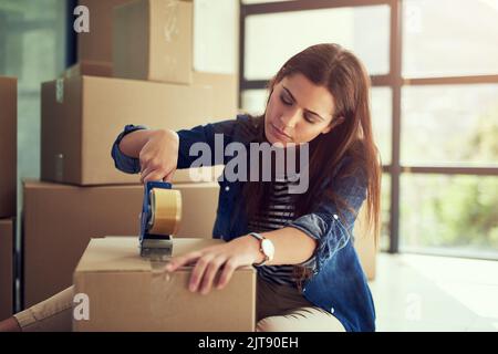 Securing the last of her things before the big move. a young woman packing boxes while moving house. Stock Photo