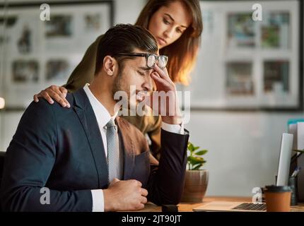 Too much pressure. a stressed out businessman being comforted while sitting at a table using a laptop. Stock Photo