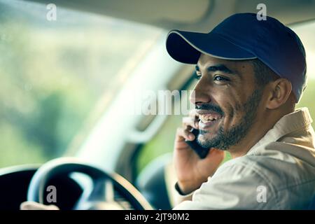 Im just a few minutes away with your delivery. a delivery man talking on a cellphone while sitting in his van. Stock Photo