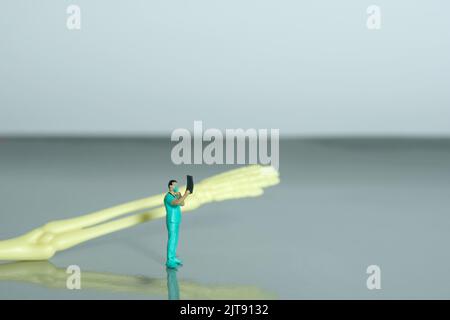 Miniature people toy figure photography. A doctor nurse looking on x ray result scan film in front of hand bone skeleton. Image photo Stock Photo