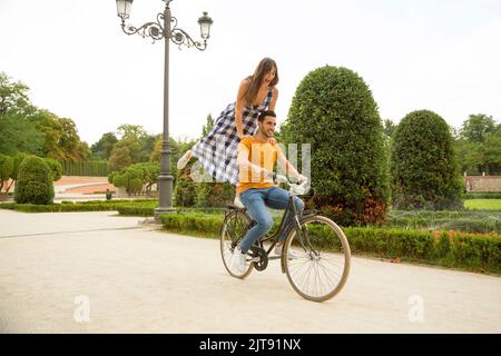 Romantic scene of a caucasian young couple doing tricks on a bike in a park Stock Photo