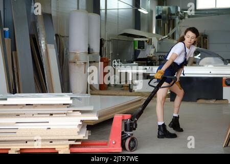 Young woman using hydraulic trolley in carpenter workshop Stock Photo