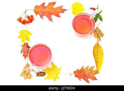 Two mugs with of hot red colored drinks framed with bright autumn leaves and berries isolated on white. Stock Photo