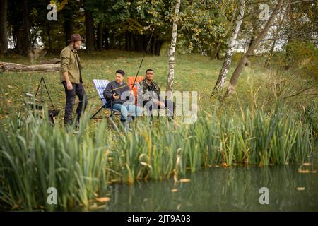 Pleased male friends resting and fishing in nature Stock Photo