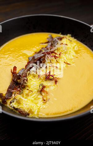 Cream of pumpkin soup with meat and cheese in a black plate on a wooden background Stock Photo