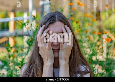 A woman covers her face with her hands, her eyes are closed Stock Photo