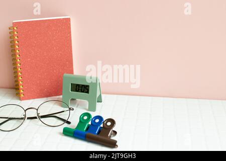 Office desk table with notebook, eyeglasses, clock, clip, supplies on white desk. pink wall background Stock Photo