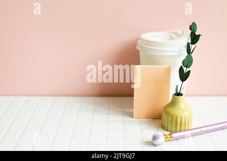 Paper coffee cup, memo pad, pen, dry plant on white desk. pink wall background Stock Photo