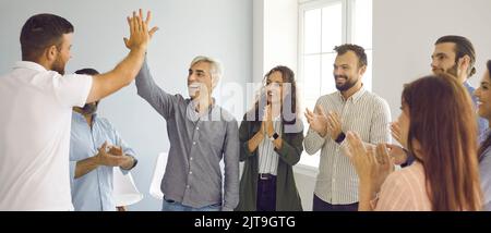 Employee giving high five to smiling senior business group leader to applause of colleagues. Stock Photo