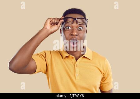 Young man opens his mouth, lifts glasses and looks at something with surprised face expression Stock Photo