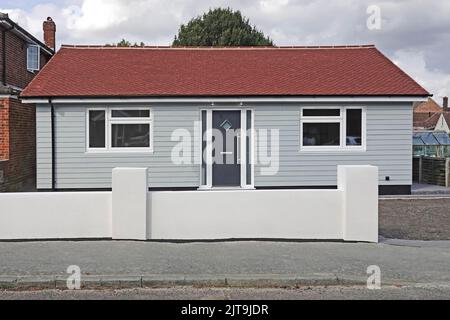 Fibre cement weather boarding on façade elevation of new* large floor area bungalow home red plain tile roof car parking behind front wall England UK Stock Photo