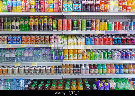 Rows of colourful soft drink cans & bottles some sugary high sugar content & co2 fizzy drinks on shelving inside convenience shop Essex England UK Stock Photo