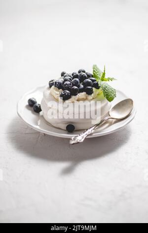Delicious mini Pavlova meringue nest with blueberry and mint leaves served on white plate Stock Photo