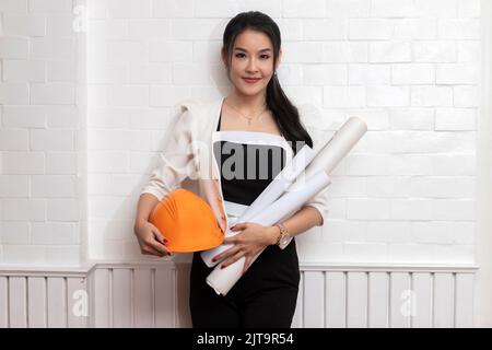 Female architect or engineer holding blueprints at the wall. Stock Photo