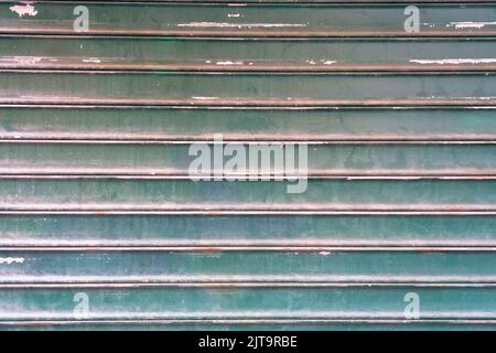 Dirty textured steel garage door painted in green, background, striped metal colored shutter wall, abstract horizontal lines, grunge texture and patte Stock Photo