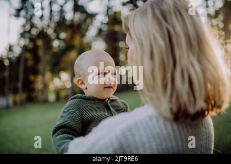 Mother holding her little baby son wearing knitted sweater during walk in nature. Stock Photo