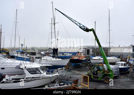 Crane lifting a mast back on to a sailing boat standing in East Llanion boatyard, East Llanion, Pembrokeshire, Wales Stock Photo