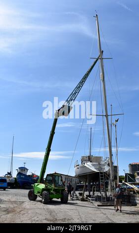 Crane lifting a mast back on to a sailing boat standing in East Llanion boatyard, East Llanion, Pembrokeshire, Wales Stock Photo