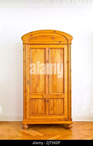 Restored vintage furniture: antique wooden wardrobe against the white wall of an old building with parquet flooring and stucco plastering, copy space. Stock Photo