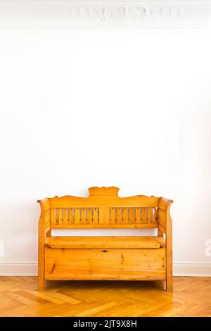 Old wooden box bench with storage space unter the seat, circa 1880, against the white wall of an old building with parquet flooring, copy space. Stock Photo