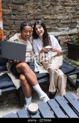 Cheerful interracial girlfriends with coffee using laptop in outdoor coffee,stock image Stock Photo