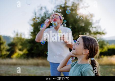 Young father and his little daughter having fun while blowing soap bubbles on a summer day in nature. Stock Photo