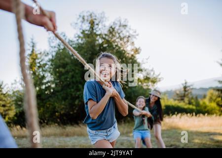 Young family with happy kids having fun together outdoors pulling rope in summer nature. Stock Photo