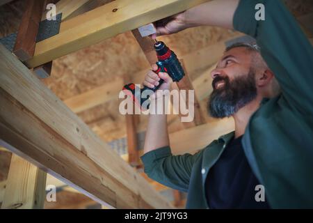 Construction worker working with screwdriver on wooden frame, diy eco-friendly homes concept. Stock Photo