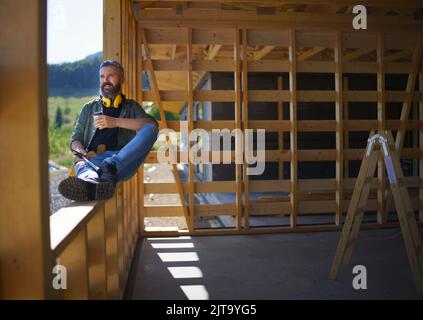 Handyman resting and having break when working on wooden construction site, diy eco-friendly homes concept. Stock Photo