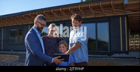 Sales Agent showing plans of new house to young family on construction site. Stock Photo