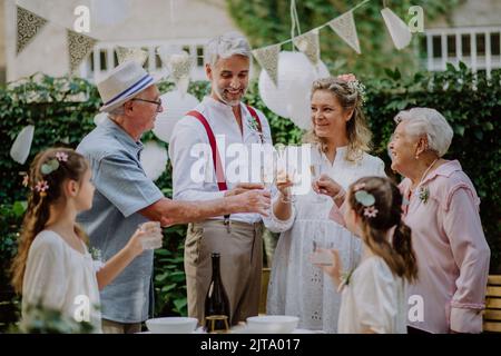 Mature bride and groom toasting with family at wedding reception outside in the backyard. Stock Photo