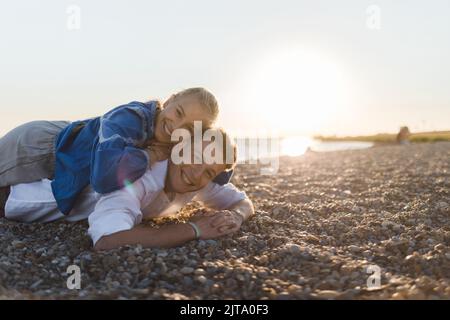 Happy young woman lying on her boyfriends back, looking at camera, having fun together. Stock Photo