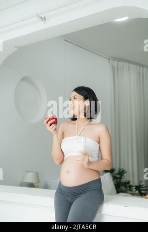 Pregnant Woman holding her pregnant belly and get a glass of milk and apple. Stock Photo