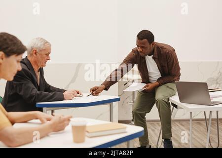 African teacher explaining how to write test to senior student during exam in classroom Stock Photo