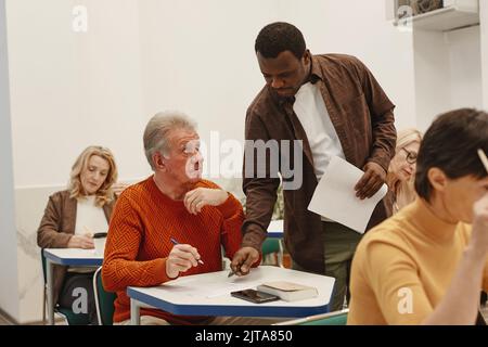 African young teacher walking along the class and explaining adult students how to write test Stock Photo