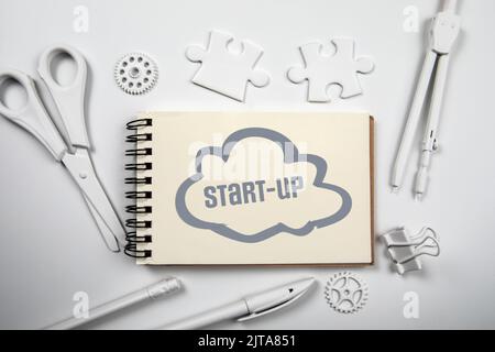 Start-Up. Text and cloud on notepad. White office desk. Stock Photo
