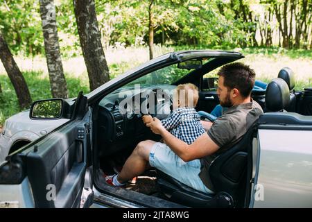 Dad shows his little son how to drive car while sitting behind wheel Stock Photo