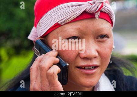 Vietnam, Red Dao tribe woman is using her mobile phone in the northern city Sapa. Stock Photo