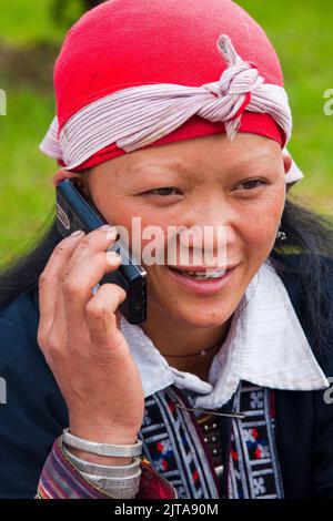 Vietnam, Red Dao tribe woman is using her mobile phone in the northern city Sapa. Stock Photo