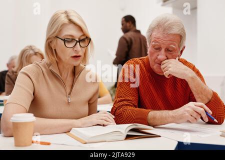 Senior couple sitting at desk and reading a book together during training in class Stock Photo