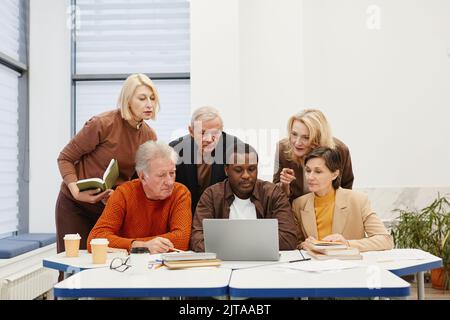 Group of senior students learning to use laptop together with teacher at desk during educational training Stock Photo