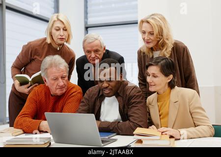 African teacher showing his senior students how to use laptop while they sitting together at desk in classroom Stock Photo