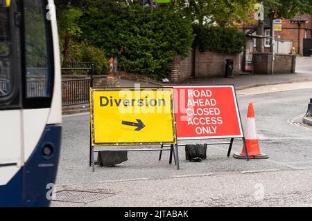 Road closed and diversion sign with a bus passing by and traffic being diverted around Winchester Road to repair a water main burst. Basingstoke, UK Stock Photo