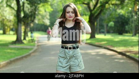 Annoyed confused millennial girl raising arms in disbelief in outdoor park. Puzzled young woman reaction Stock Photo