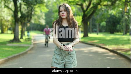 Annoyed confused millennial girl raising arms in disbelief in outdoor park. Puzzled young woman reaction Stock Photo