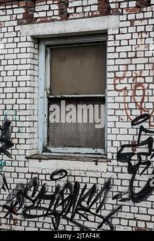 Old boarded up window in a white brick wall with graffitti Stock Photo