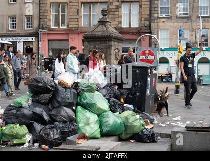 Edinburgh, Scotland, UK. 29th August 2022. Edinburgh bin men strike in second week and the city’s streets are covered in litter from overflowing rubbish bins. Pic; Tourists on city walking tour pass large pile of rubbish in the Grassmarket. Iain Masterton/Alamy Live News Stock Photo